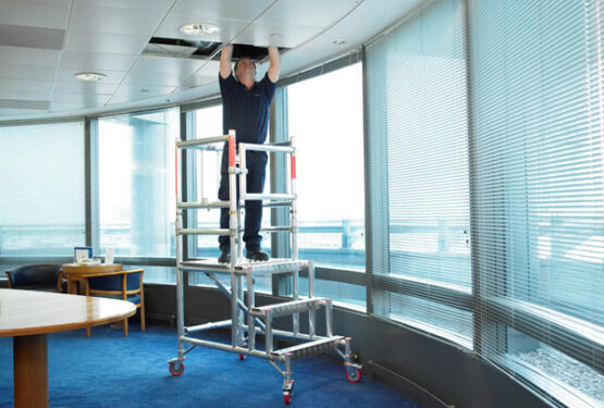 Man in office building standing on a low level working platform equipment doing working to the ceiling.