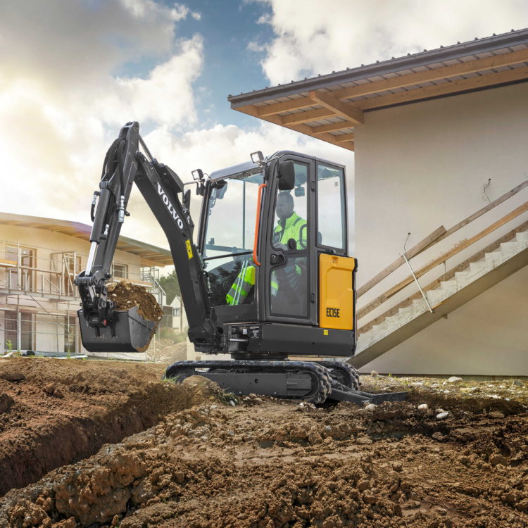 Mini excavator digging a trench beside a building under construction.