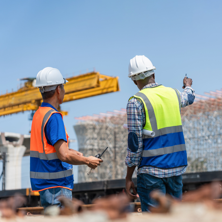 Two construction workers coordinating a crane lifting operation using radio communication on a construction site.